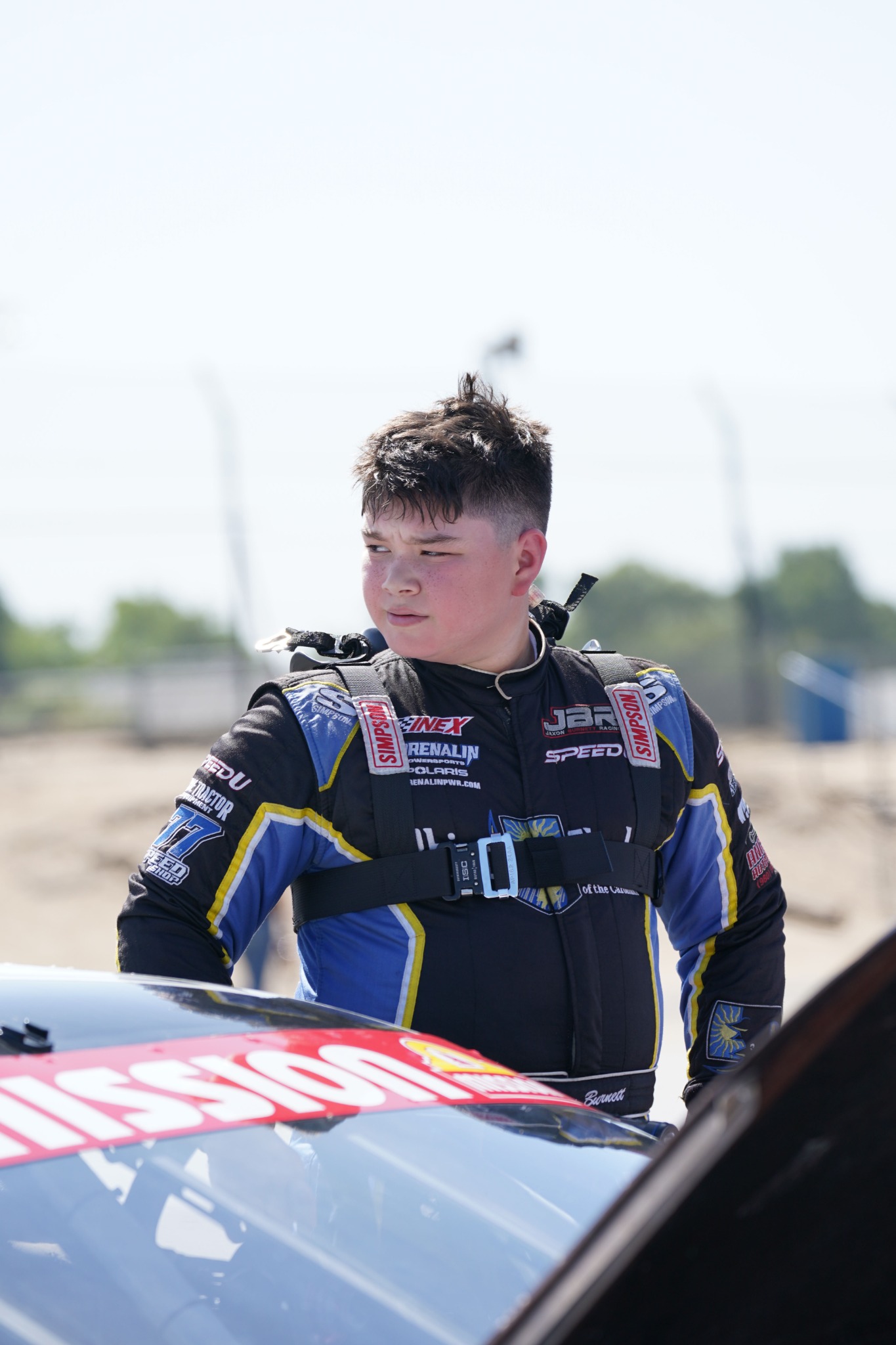 Jaxon Burnett in his racing suit beside his race car