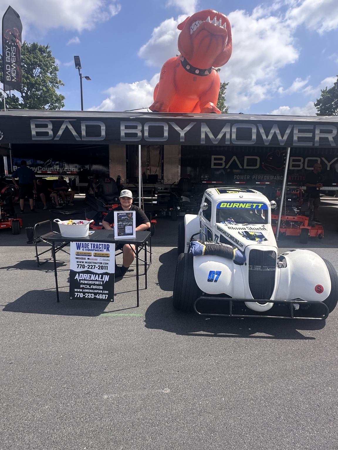 Jaxon beside his Legend car and Wade Tractor and Adrenalin Powersports display